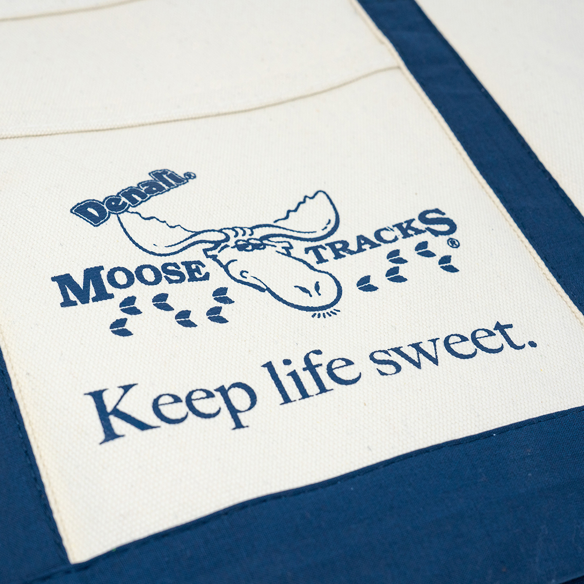 A close-up shot of the Moose Tracks canvas tote bag, with navy detailing and a navy Moose Tracks logo and "Keep Life Sweet" screen printed in the middle.