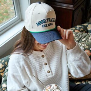 A woman is wearing a Moose Tracks Two-Tone Rope Hat, looking down and smiling at a cup of ice cream.